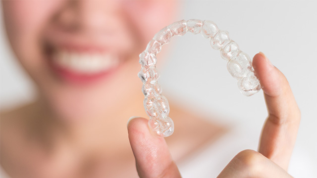 A person holding up a set of clear dental aligners with a smile.