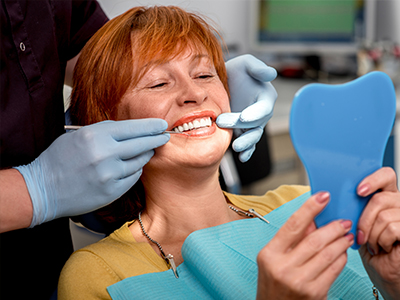 The image shows a woman with red hair sitting in a dental chair, receiving dental care from a professional wearing blue gloves and a white mask.