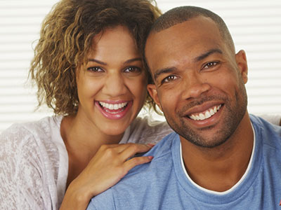 A man and woman posing together with smiles on their faces, appearing happy and embracing each other.