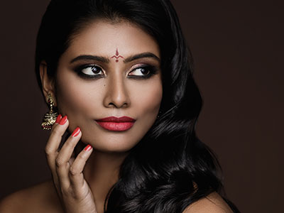 The image features a woman with dark hair, wearing makeup and jewelry, posing for a portrait with her hand near her face.