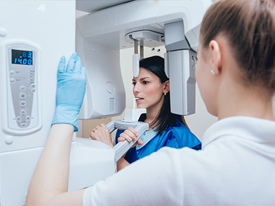 A woman operating a large, modern 3D scanner machine while another person looks on, both wearing gloves and protective eyewear.