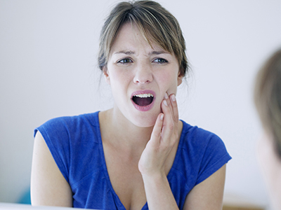 The image shows a woman with her mouth open, expressing surprise or shock, while looking at her reflection in a mirror.