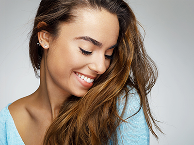 A young woman with long hair smiles and looks down towards her shoulder.