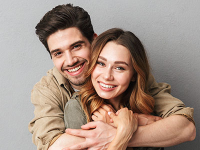 A man and woman are embracing each other with smiles, posing for a portrait-style photograph.