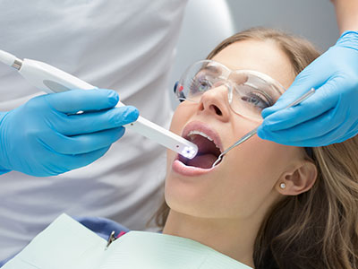 The image shows a dental professional using an electric toothbrush on a patient s teeth during a dental cleaning appointment.