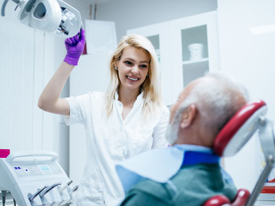 A smiling dental hygienist assisting an older man with a medical device during a dental procedure.