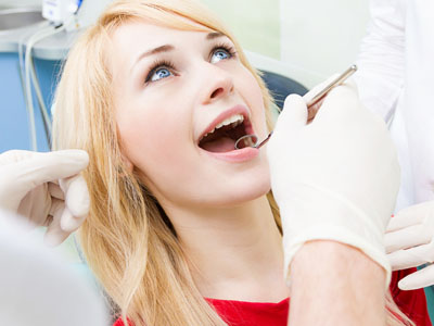 A woman receiving dental care, with a dentist performing an examination using a dental mirror.