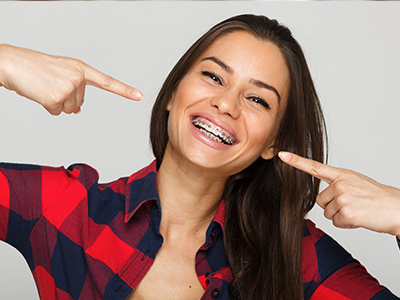 A smiling woman pointing at her teeth with both hands.