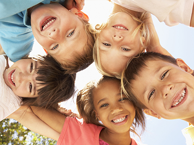 A group of children of various ages smiling together outdoors.