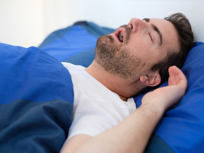 A man lying down in bed with his eyes closed, appearing to be asleep.