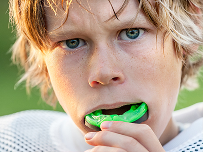 A young person with blonde hair brushing their teeth with a toothbrush.