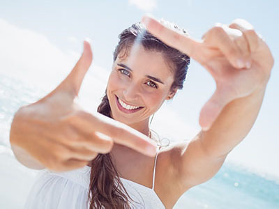 Woman holding up two fingers against bright sky with sun glare effect.