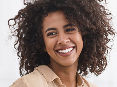 The image features a smiling woman with curly hair, wearing a light-colored top, against a neutral background.